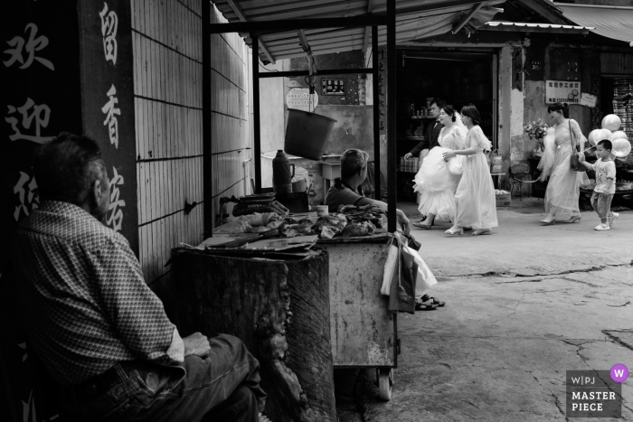 Photo by: <a href="https://www.wpja.com/contests/2019-v07/best-wedding-photographers/2505656">Joy Qin - Longyan </a> A man watches the wedding party proceed from afar in this black and white wedding image by a documentary Fujian, China photographer.