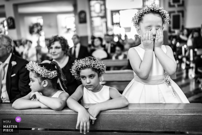 Photo by: <a href="https://www.wpja.com/contests/2019-v07/best-wedding-photographers/2505851">Federica Ariemma - Napoli Napoli</a> A girl covers her face while two others watch the ceremony in Lettere in this black and white photo by a Naples, Campania wedding photographer.