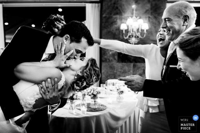 Guests smile and cheer as the groom kisses the bride during their reception at El Puig in this black and white image composed by an award-winning Valencia, Spain wedding photographer.