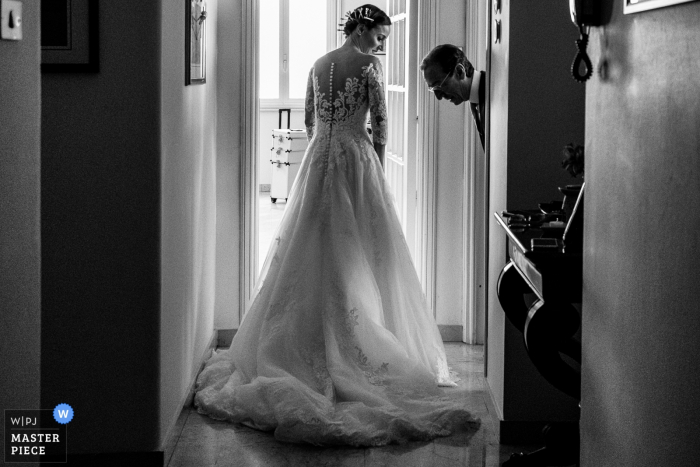 Zdjęcie: <a href="https://www.wpja.com/contests/2019-v07/best-wedding-photographers/2506671"> Salvo Moroni - Viagrande Catania </a> Mężczyzna bada suknię panny młodej przed ślubem w San Francesco all'Immacolata na tym czarno-białym zdjęciu autorstwa fotografki z Katanii na Sycylii.