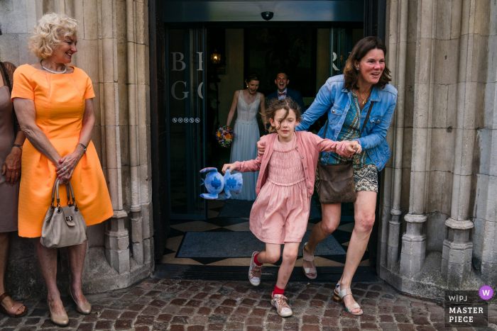 A little girl and her mother run out of the Brugge Town Hall in La Petite Fabriek in this wedding photo by a Flanders photographer.