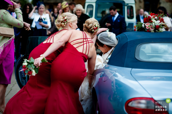 La ferme, Cambridgeshire, Royaume-Uni demoiselles d'honneur aidant la mariée hors de la voiture - Reportage de mariage