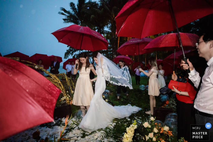 Foto: <a href="https://www.wpja.com/contests/2019-v07/best-wedding-photographers/2507881"> Leon Wong - Hangzhou </a> Ritz-Carlton, Krabi, Thailand Hochzeitszeremoniephotographie in einem Regensturm mit roten Regenschirmen