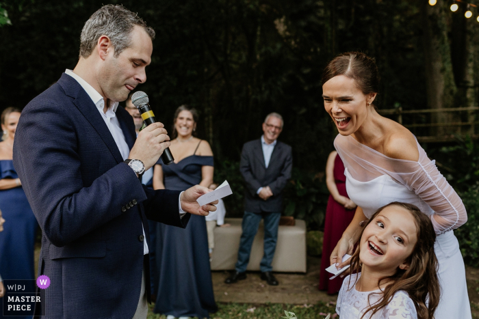 Photo by: <a href="https://www.wpja.com/contests/2019-v07/best-wedding-photographers/2507916">Renan Radici - Porto Alegre Rio Grande do Sul</a> The bride and a little girl laugh as a man gives a speech during this wedding at Casa dos Novios by a Porto Alegre award-winning photographer.