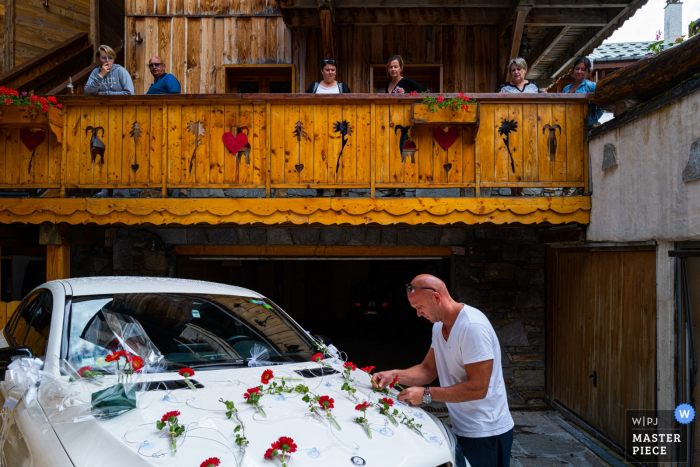 An seinem Hochzeitstag in den französischen Alpen schmückt der Bräutigam das Auto vor den Gästen.