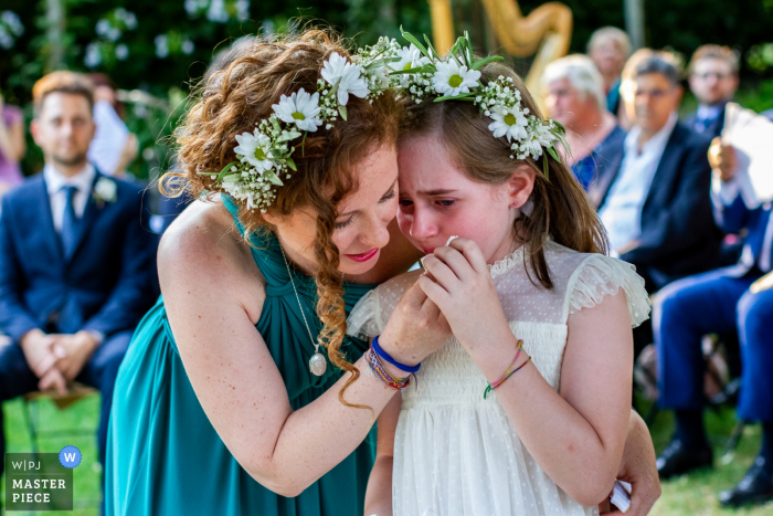 Una mujer limpia las lágrimas de una niña llorando durante la ceremonia en I Giardini di Villa Fago, Santa Venerina, en esta imagen de estilo documental compuesta por un fotógrafo de bodas de Catania, Sicilia.