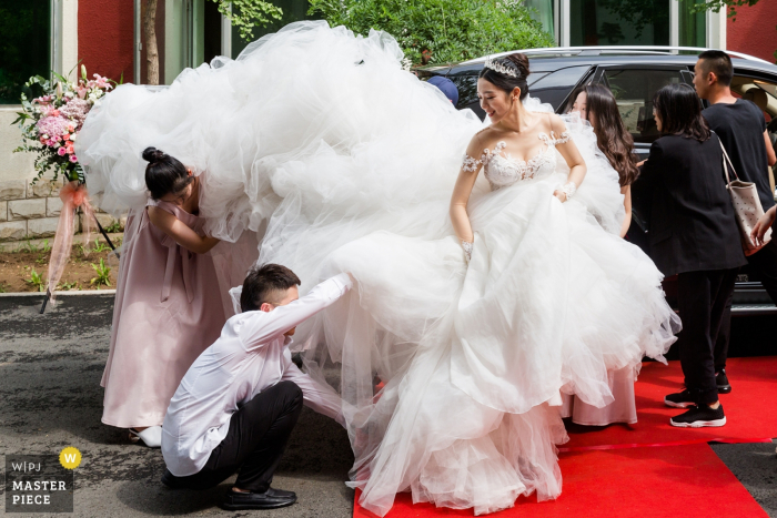 Photo by: <a href="https://www.wpja.com/contests/2019-v08/best-wedding-photographers/2511861">Xiaozhu Lin - Beijing </a> A few guests try to help the bride with her gigantic wedding dress outside of Beijing Yunheyuandujiacun Hotel in this award-winning wedding image by a Beijing, China photographer.