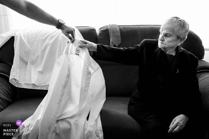 Photo by: <a href="https://www.wpja.com/contests/2019-v08/best-wedding-photographers/2512646">Antonio Calatayud - La Eliana Valencia</a> A guest hands the groom his shirt while he gets ready before his Albacete wedding in this black and white image composed by a Valencia, Spain wedding photographer.