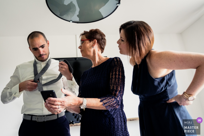 Foto por: <a href="https://www.wpja.com/contests/2019-v08/best-wedding-photographers/2512911"> Caroline Elenbaas - Heijningen Noord Brabant </a> El novio no tiene idea de cómo arreglar su corbata e intenta buscar instrucciones antes de su boda en Bovendonk, Hoeven, en esta imagen creada por un fotógrafo de bodas de Noord Barbant, Países Bajos.