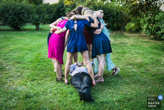 Photo by: <a href="https://www.wpja.com/contests/2019-v08/best-wedding-photographers/2513846">Ronan Jégaden - Athis-Mons </a> Women huddle together as a man lays on the ground and takes a picture of them from below in this award-winning photo composed by a Paris, France wedding photographer.