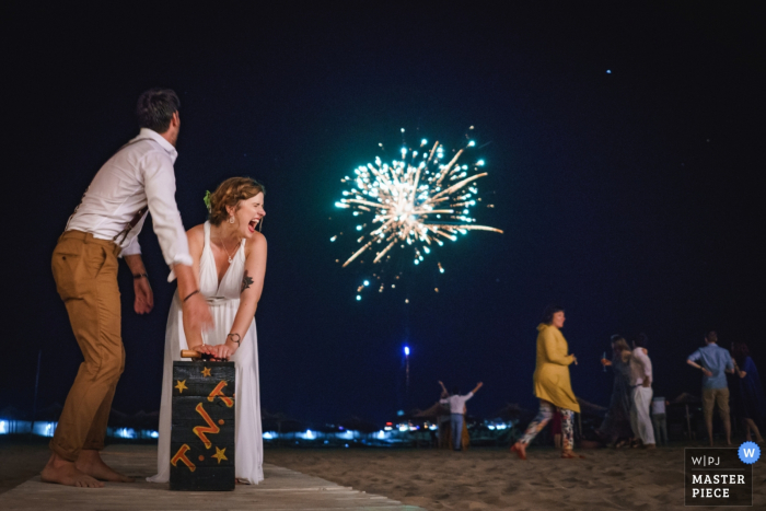 Photo by: <a href="https://www.wpja.com/contests/2019-v08/best-wedding-photographers/2514281">Boni Bonev - Sofia Sofia</a> The bride pushes the lever on a box marked "T.N.T." to light a firework at Perla Beach, Primorsko in this wedding image composed by an award-winning Sofia, Bulgaria photographer.