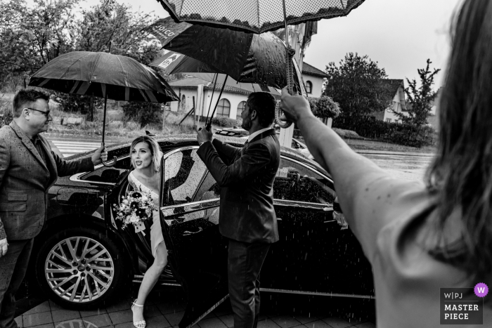 Photo by: <a href="https://www.wpja.com/contests/2019-v08/best-wedding-photographers/2514981">Philippe Swiggers - Bekkevoort </a> Guests hold umbrellas over the bride as she exits her vehicle at Gemeentehuis Glabbeek in this black and white wedding photo captured by a Flanders, Belgium photographer.