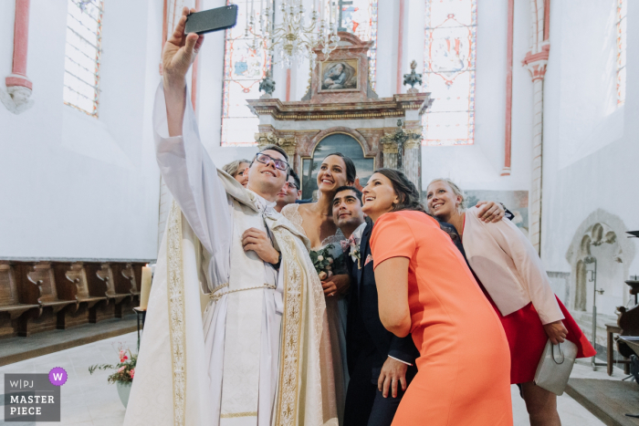 Foto von: <a href="https://www.wpja.com/contests/2019-v08/best-wedding-photographers/2515131"> Christophe Pasteur - Lorient </a> Der Priester macht ein Selfie mit der Brautparty in der Kirche von La Chatelet En Brie auf diesem Bild, das von einem preisgekrönten Hochzeitsfotografen aus Morbihan, Bretagne, aufgenommen wurde.