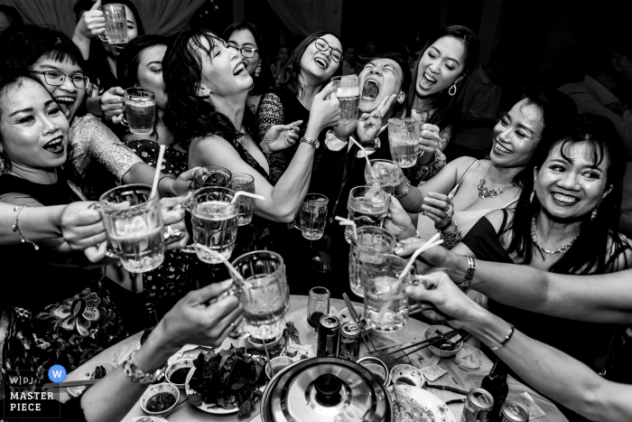 Un groupe d'invités avec un seul homme partageant un verre ensemble au restaurant Zenna sur cette photo en noir et blanc réalisée par un photographe de mariage à Ho Chi Minh, au Vietnam.