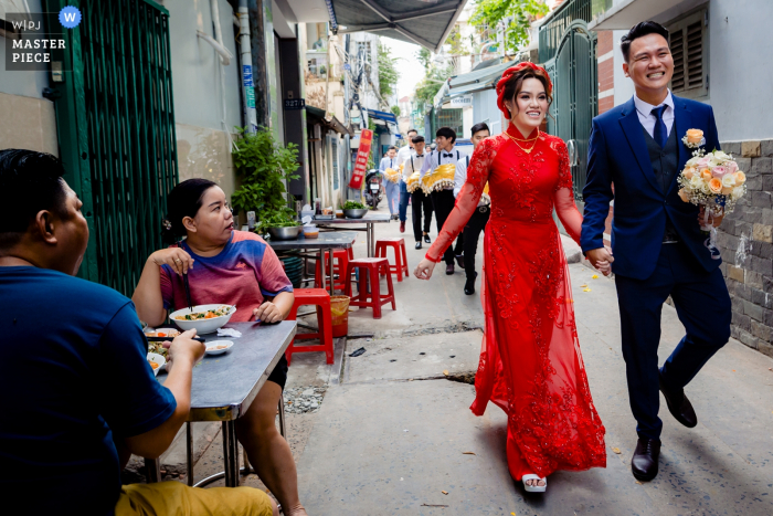 Photo par: <a href="https://www.wpja.com/contests/2019-v08/best-wedding-photographers/2517546"> Tuan Duong - Hô Chi Minh </a> Les mariés se tiennent la main alors qu'ils sont suivis par une procession alors qu'ils rentrent chez eux dans cette image de style documentaire capturée par un photographe de mariage à Ho Chi Minh, au Vietnam.