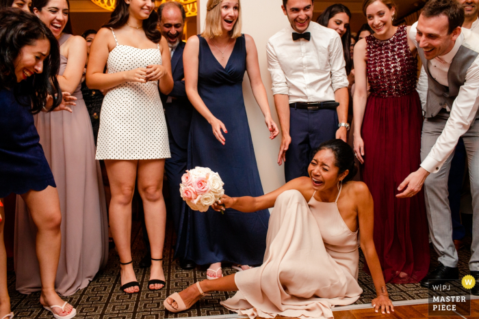 Foto por: <a href="https://www.wpja.com/contests/2019-v08/best-wedding-photographers/2517631"> Siliang Wang - San Jose California </a> Todos se ríen cuando una invitada trata de ponerse de pie después de que ella se cayera tratando de recoger el ramo en el hotel Palo Alto Garden Court en esta imagen de boda compuesta por un fotógrafo de San José, California.