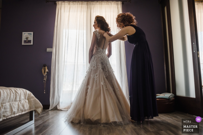 Photo by: <a href="https://www.wpja.com/contests/2019-v08/best-wedding-photographers/2518326">Ivelina Cholakova - Sofia Sofia</a> A woman helps the bride close the back of her dress in the final countdown to the ceremony in this award-winning image composed by a Sofia, Bulgaria wedding photographer.