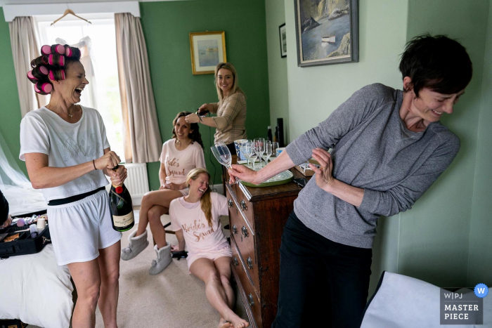 Maison des parents des mariées pendant les préparatifs du matin. Cambridgeshire, Royaume-Uni Mariage dans les tipis dans le jardin des parents de la mariée, la soeur de la mariée veut éviter toute blessure alors que la mariée ouvre avec enthousiasme la première bouteille de champagne