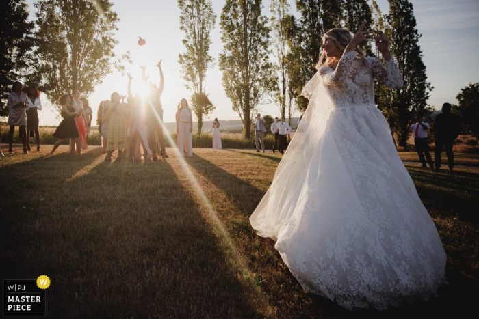 Photo by: <a href="https://www.wpja.com/contests/2019-v08/best-wedding-photographers/2518786">Simon Cassanas - Paris </a> The bride tosses her bouquet over her shoulder as the sun sets at Clos de L'Orangerie Rosney Sur Seine in this documentary-style wedding photo by an award-winning Paris, France photographer.