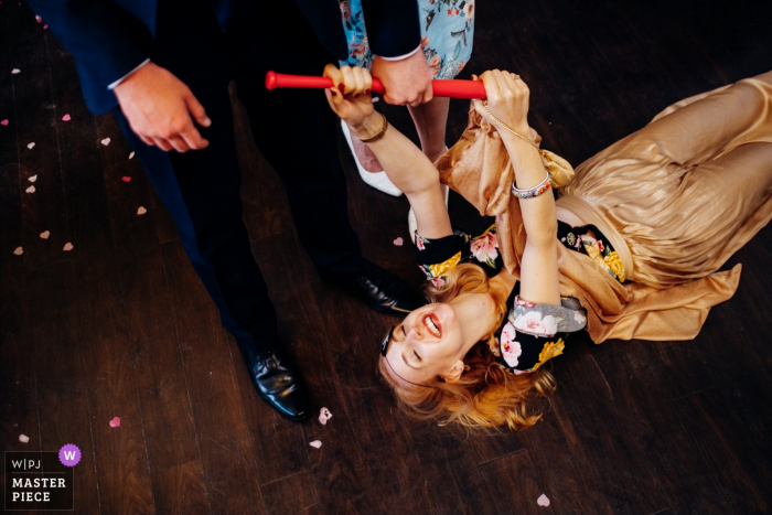 A woman holds onto a red baseball bat while she lays on the floor of Morden Hall in this wedding photo captured by a London, England documentary photographer.