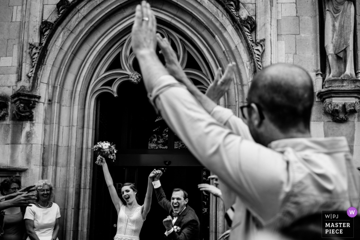 Photo by: <a href="https://www.wpja.com/contests/2019-v08/best-wedding-photographers/2520181">Nathalie Moors - Dessel Antwerpen</a> The bride and groom exit their ceremony in Brugge with their arms raised in this black and white picture captured by an Antwerpen, Flanders documentary-style wedding photographer.