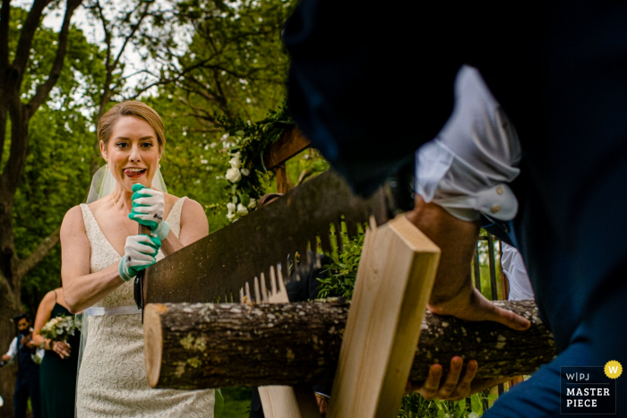 Photo by: <a href="https://www.wpja.com/contests/2019-v08/best-wedding-photographers/2520541">Ilana Bar-av - Madison Wisconsin</a> Hubbard Park Shorewood Wisconsin Wedding Photo showing the Bride and Groom do a sawing tradition - Madison, WI photographer
