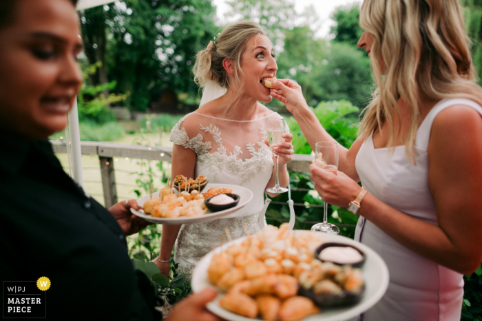 A guest feeds the bride a bite of food during her reception at the mill A guest feeds the bride a bite of food during her reception at Tuddenham Mill, UK in this image taken by a West Midlands, England wedding photographer.