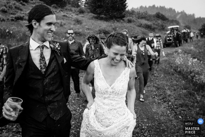 Photo by: <a href="https://www.wpja.com/contests/2019-v09/best-wedding-photographers/2530641">David Clumpner - Missoula Montana</a> Black and white wedding shot of the newlywed couple walking through rain with guests following at Mountain Top near Bozeman, MT