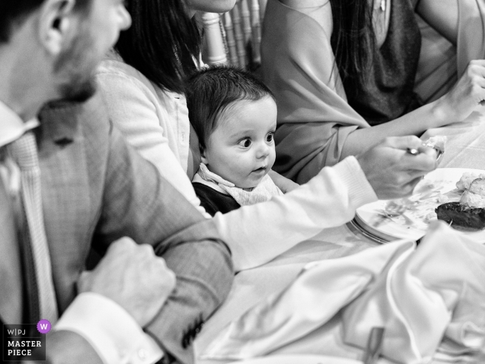 Photo by: <a href="https://www.wpja.com/contests/2019-v09/best-wedding-photographers/2534116">Michela Bocciarelli - Milano Milano</a> Ville Ponti, Varese wedding photograph of a young child sitting in the lap of his mother at a wedding reception table.