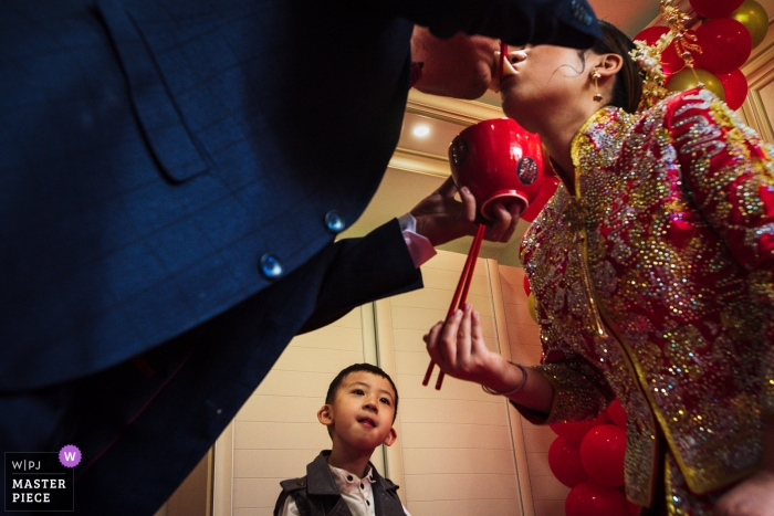 Photo by: <a href="https://www.wpja.com/contests/2019-v09/best-wedding-photographers/2536006">Moana Wu - Shanghai </a> Chinese wedding tradition of bride and groom eating noodles as young boy watches intentively in Liaoning, China