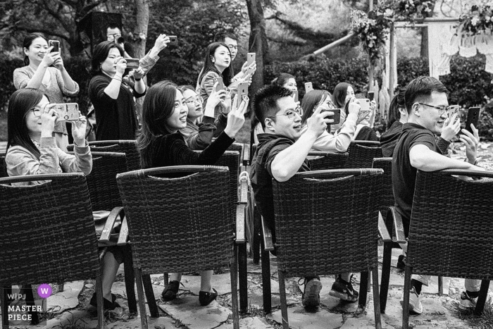 Imagen en blanco y negro de los invitados a la boda de Beijing tomando fotos con sus dispositivos móviles.