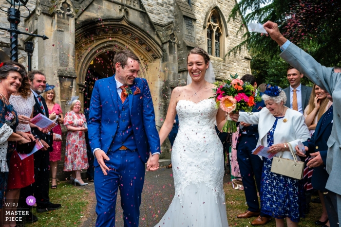 Zdjęcie: <a href="https://www.wpja.com/contests/2019-v09/best-wedding-photographers/2539546"> Paul Tansley - Bordon Hampshire </a> Kościół parafialny St. Mary's Ewell - Fotografia ślubna rzutu konfetti - Pan młody bierze ciężar konfetti - para idzie w naszym kierunku