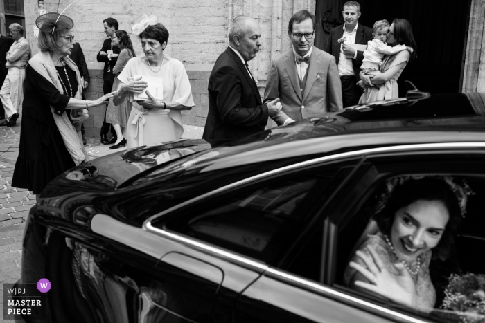 Photo by: <a href="https://www.wpja.com/contests/2019-v10/best-wedding-photographers/2542491">Joshua Dhondt - Antwerpen</a> Bride waves to her friends as she leaves in a car, and her guests hang out at the Kasteel van Ruisbroek.