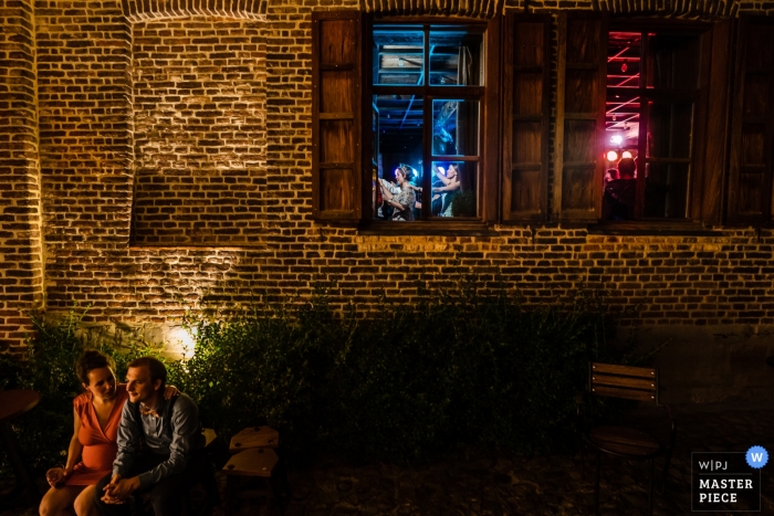 Photo by: <a href="https://www.wpja.com/contests/2019-v10/best-wedding-photographers/2543760">Simon Leclercq - Leuven Vlaams Brabant</a> La Petite Fabriek wedding photograph of a couple enjoying a break outside the reception hall while you get a glimpse of the party inside.