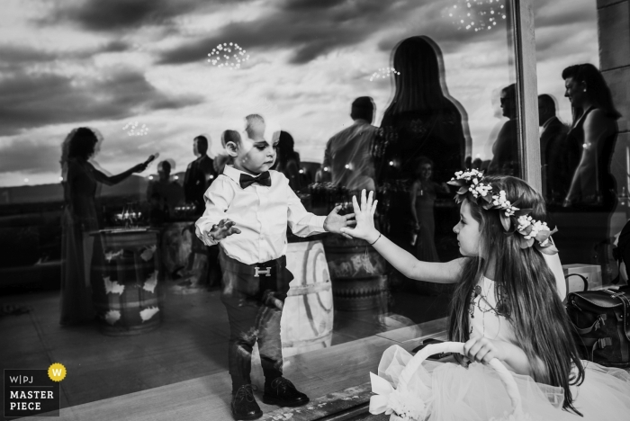 Zdjęcie: <a href="https://www.wpja.com/contests/2019-v11/best-wedding-photographers/2544457"> Boni Bonev - Sofia Sofia </a> Katarzhina Estate, Svilengrad, Bułgaria Fotografia ślubna dzieci dotykających rąk przez szkło w recepcji.