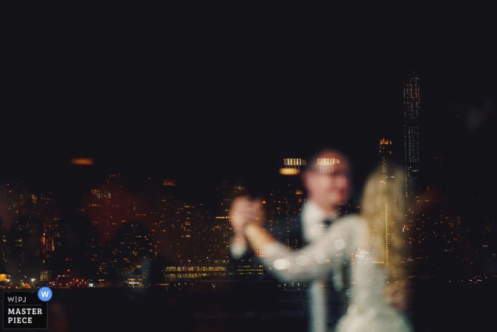 Photo by: <a href="https://www.wpja.com/contests/2019-v11/best-wedding-photographers/2544467">Ashley Davenport - Castle Dongington Derbyshire</a> New York wedding photo of a first dance taken through a window reflecting the New York sky line.