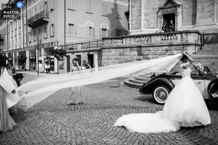 Damas de honra ajudam a noiva com seu véu nas ruas em seu casamento em Bellinzona.