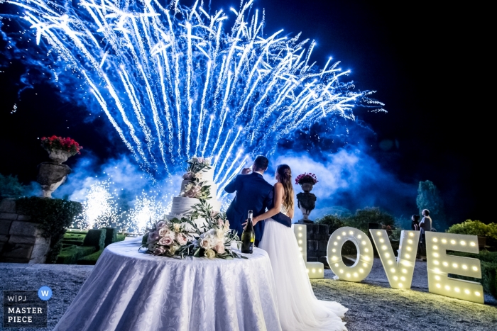 Fotografia de recepção de casamento Villa Orsini Colonna da noiva e do noivo assistindo fogos de artifício azuis com o bolo de casamento em primeiro plano.