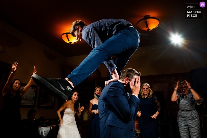 Photo by: <a href="https://www.wpja.com/contests/2019-v11/best-wedding-photographers/2544695">Stacy Gillespie - Silverthorne Colorado</a> Uley's Cabin, Crested Butte wedding reception photo of a man leaping over the head of another man.