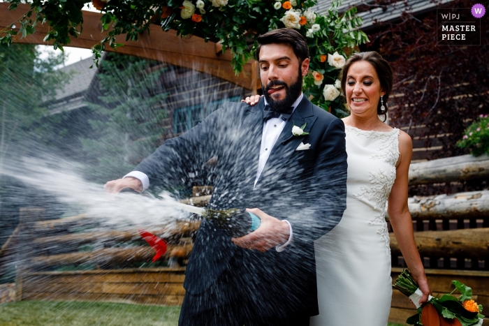 Photo by: <a href="https://www.wpja.com/contests/2019-v11/best-wedding-photographers/2544697">Stacy Gillespie - Silverthorne Colorado</a> Wedding image of a bride with her groom taking the top of a bottle of champagne at their Ritz Carlton, Beaver Creek wedding.