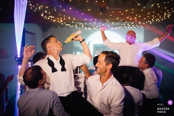 Foto von: <a href="https://www.wpja.com/contests/2019-v11/best-wedding-photographers/2544997"> Julian Kanz - Portofino Genova </a> Foto des Bräutigams und seines Vatis auf den Schultern anderer Gäste, die Limoncello an einem Castello di Meleto, Toskana trinken