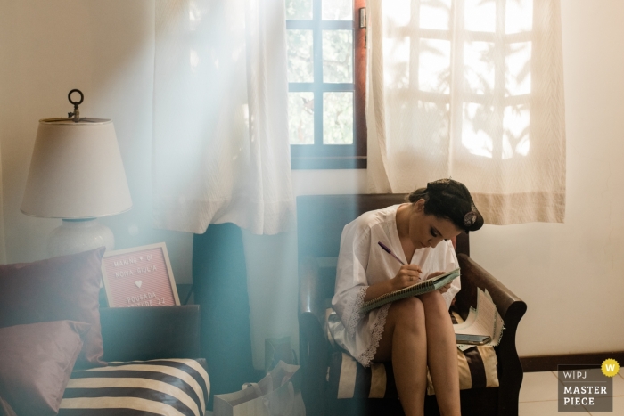 Zdjęcie: <a href="https://www.wpja.com/contests/2019-v11/best-wedding-photographers/2545100"> Aline Prado - Macaé Rio de Janeiro </a> Zdjęcie panny młodej siedzącej i piszącej przed ślubem w Rio de Janeiro.