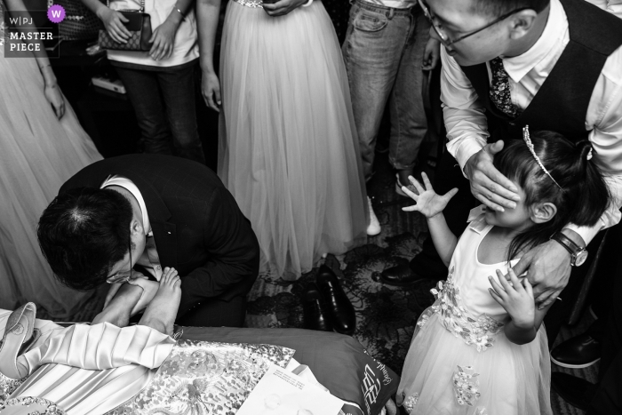 Photo by: <a href="https://www.wpja.com/contests/2019-v11/best-wedding-photographers/2545101">XiangJie Hao - Xi'an City </a> This is the moment the dressed flower girl sees the bridegroom kissing the bride's foot. The moment he sees the bride kiss the bride's foot becomes a little shy. The best man goes to help the flower girl cover her eyes.