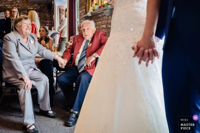 Zdjęcie: <a href="https://www.wpja.com/contests/2019-v11/best-wedding-photographers/2545796"> Freek Nagtzaam - 's-Hertogenbosch Noord Brabant </a> De Recerse Hoeve fotografia z panną młodą, panem młodym trzymającym się za ręce i obserwującymi starszych gości