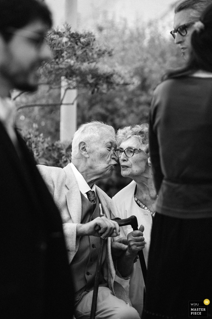 Photo by: <a href="https://www.wpja.com/contests/2019-v11/best-wedding-photographers/2546414">Jeremy Fiori - Angers </a> In front of the main hall in the town of Tierce - France Wedding Photographer | A kiss between the grandparents's of the groom