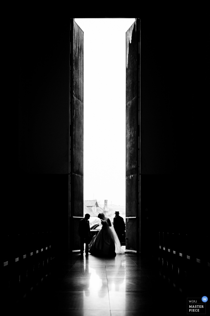 Photo by: <a href="https://www.wpja.com/contests/2019-v11/best-wedding-photographers/2546488">Daniel Monteiro - Porto </a> Black and white vertical image of the bride entering through the tall doors of the Vila Nova de Gaia for her wedding.
