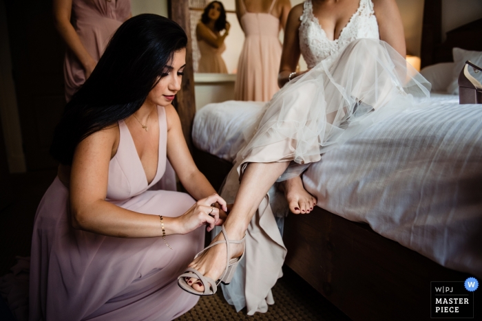 Zdjęcie: <a href="https://www.wpja.com/contests/2019-v11/best-wedding-photographers/2546576"> Megan Hannah - Lincoln Vermont </a> Sugarbush Resort w Warren, fotograf ślubny w Vermont - druhna pomaga pannie młodej w butach.