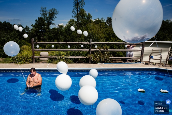 Photo by: <a href="https://www.wpja.com/contests/2019-v11/best-wedding-photographers/2546590">Jacob Hannah - Lincoln Vermont</a> Home in Middlebury, VT wedding photography - The brides dad helps set up balloons in the pool for their backyard wedding