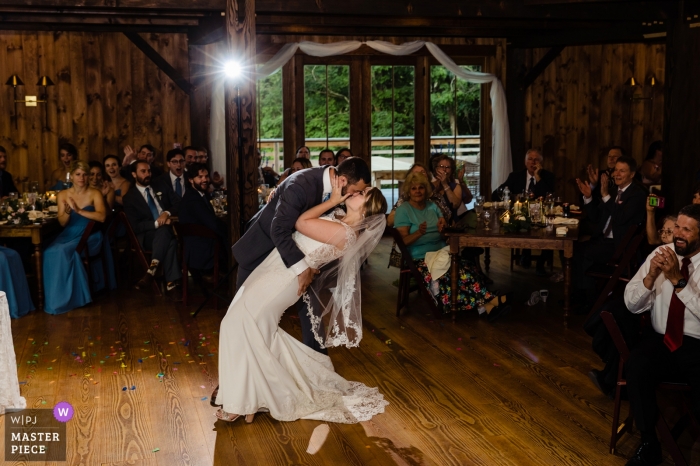 Zdjęcie: <a href="https://www.wpja.com/contests/2019-v11/best-wedding-photographers/2546612"> Sarah V. Martinez - Dover New Hampshire </a> Pan młody zanurza pannę młodą i całuje ją pocałunkiem, gdy rodzina i przyjaciele kibicują im w The Preserve at Chocorua w Tamworth, NH