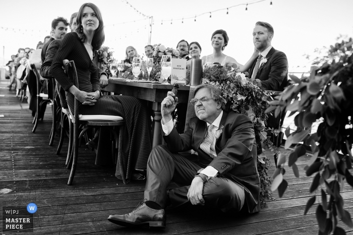 Zdjęcie: <a href="https://www.wpja.com/contests/2019-v11/best-wedding-photographers/2546682"> Tara Theilen - Carson City Nevada </a> West Shore Cafe, Homewood, Kalifornia Fotografia weselna - ojciec panny młodej uważnie filmuje przemowę swojej żony.